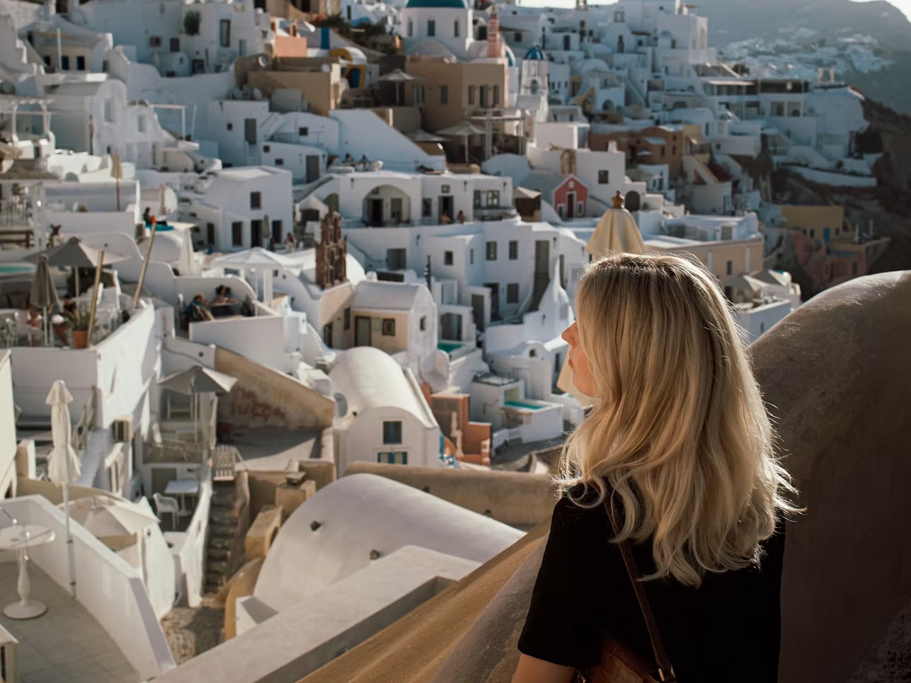 A traveler overlooking white hillside buildings and a blue-domed church in Santorini