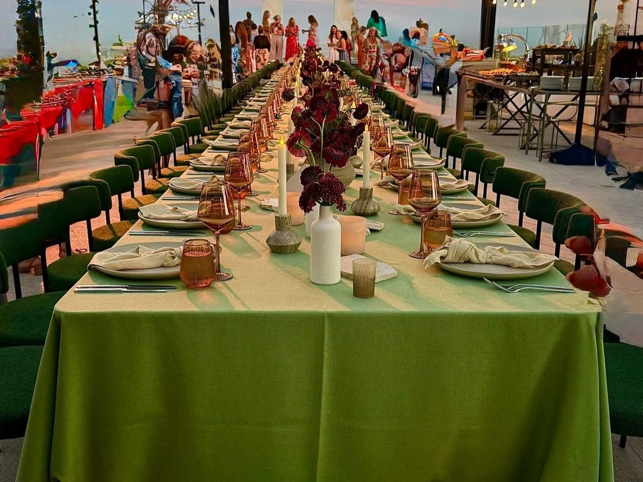 A long candlelit dinner table set for a group event at sunset